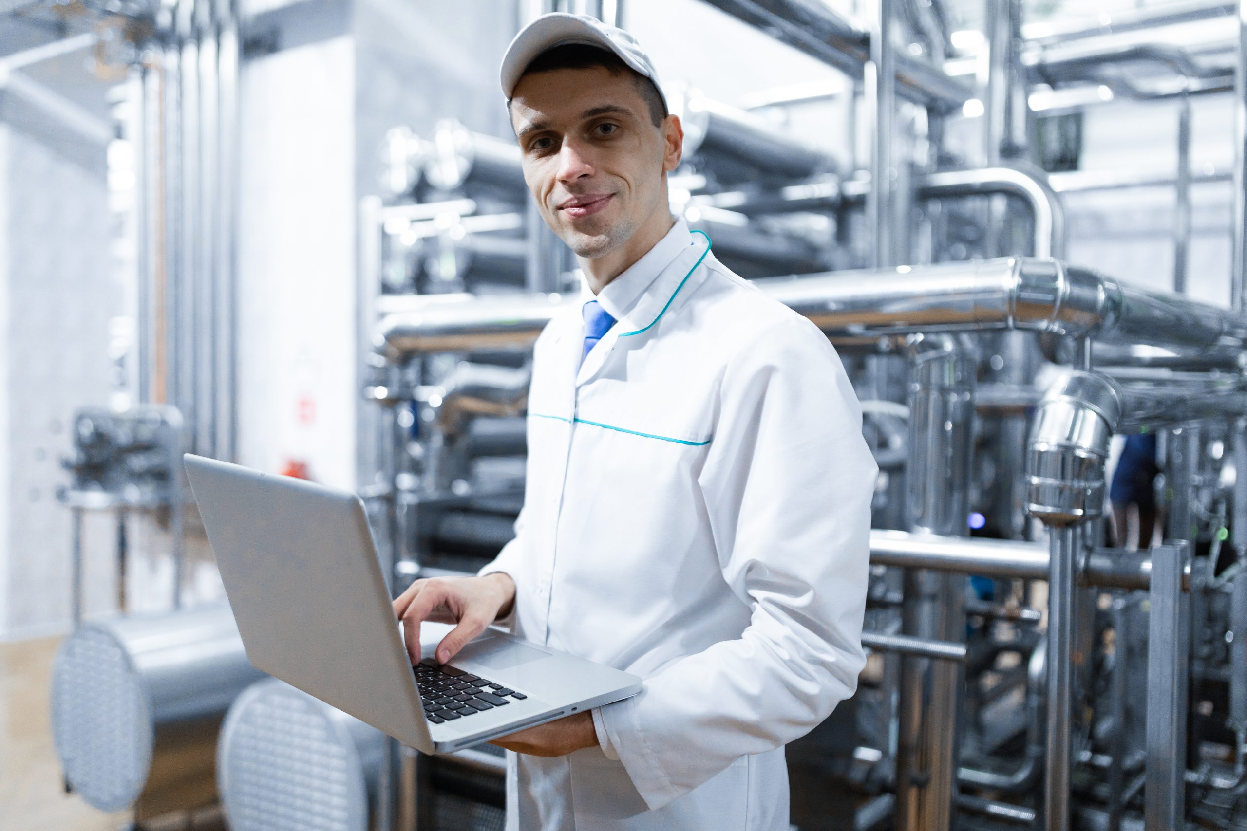 technologist with laptop in his hands make a set up of the production line while standing at the department of dairy factory